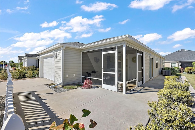 exterior space with central air condition unit, a garage, and a sunroom