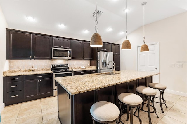 kitchen with lofted ceiling, stainless steel appliances, hanging light fixtures, and an island with sink