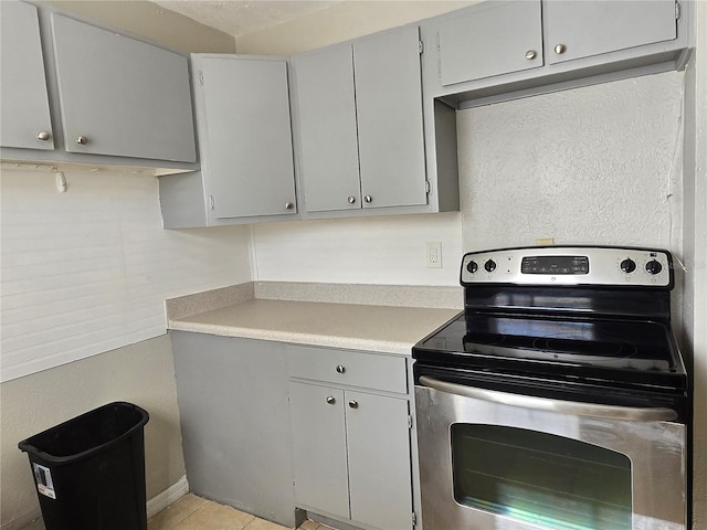 kitchen featuring stainless steel electric stove, gray cabinets, and light tile patterned floors