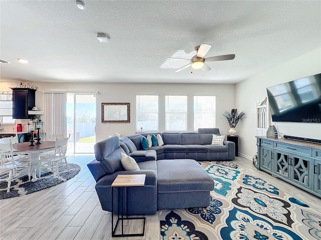 living room featuring a textured ceiling, light wood-type flooring, and ceiling fan