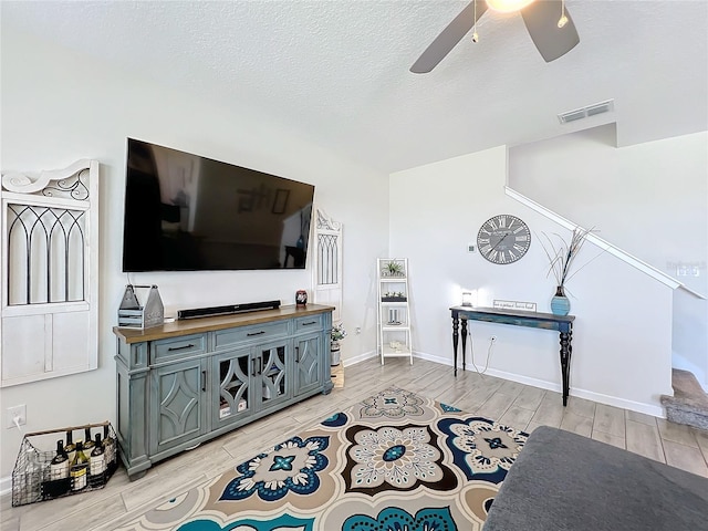 living room with ceiling fan, light hardwood / wood-style floors, and a textured ceiling