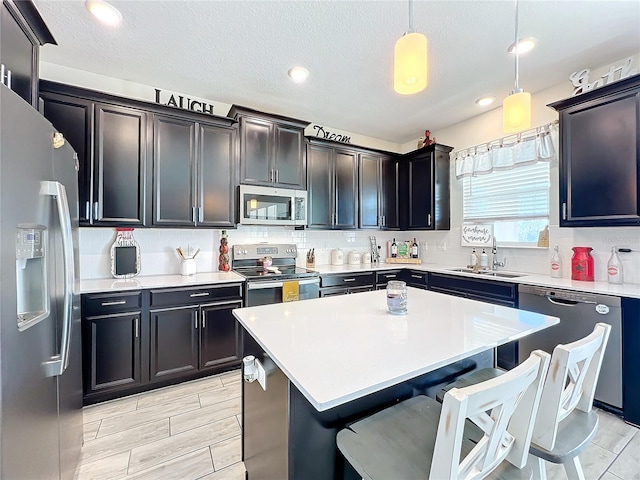 kitchen with a textured ceiling, stainless steel appliances, sink, a kitchen island, and hanging light fixtures