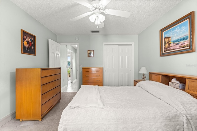 bedroom with ceiling fan, light colored carpet, a textured ceiling, and a closet