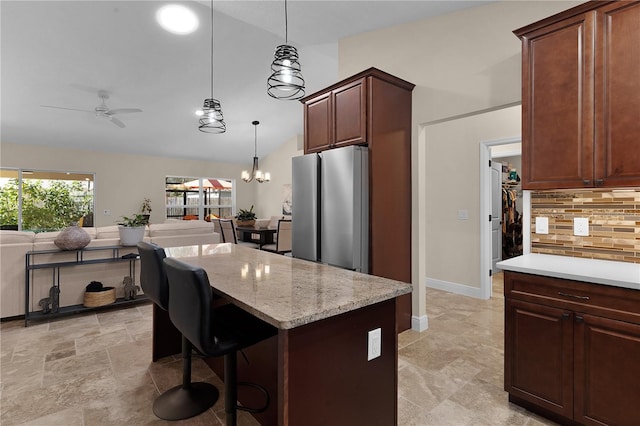 kitchen with a kitchen island, hanging light fixtures, freestanding refrigerator, tasteful backsplash, and a kitchen bar