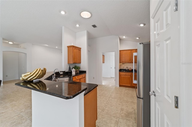 kitchen with sink, stainless steel fridge, dark stone countertops, vaulted ceiling, and kitchen peninsula