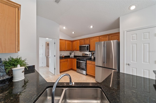 kitchen featuring sink, appliances with stainless steel finishes, dark stone countertops, a textured ceiling, and vaulted ceiling