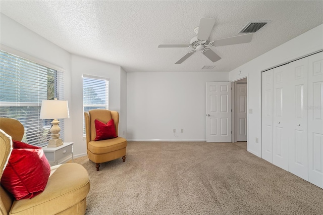 living area featuring ceiling fan, carpet floors, and a textured ceiling