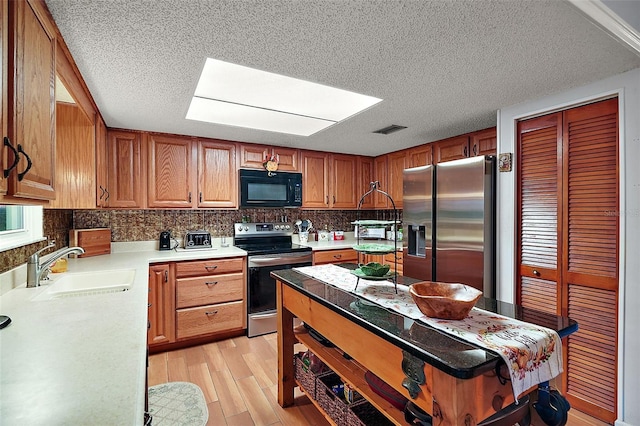 kitchen with a skylight, sink, a textured ceiling, appliances with stainless steel finishes, and light wood-type flooring