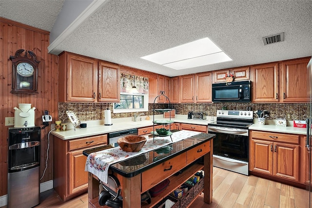 kitchen with a skylight, light wood-type flooring, a textured ceiling, and appliances with stainless steel finishes