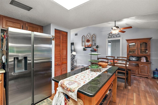 kitchen featuring ceiling fan, stainless steel fridge, a textured ceiling, a kitchen island, and dark hardwood / wood-style flooring