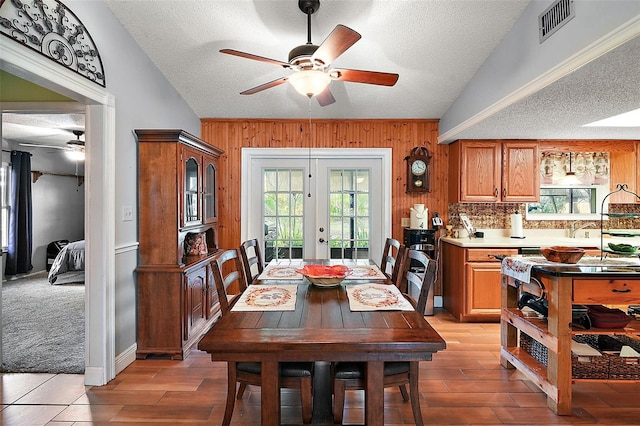 dining space featuring ceiling fan, french doors, wood walls, light colored carpet, and a textured ceiling