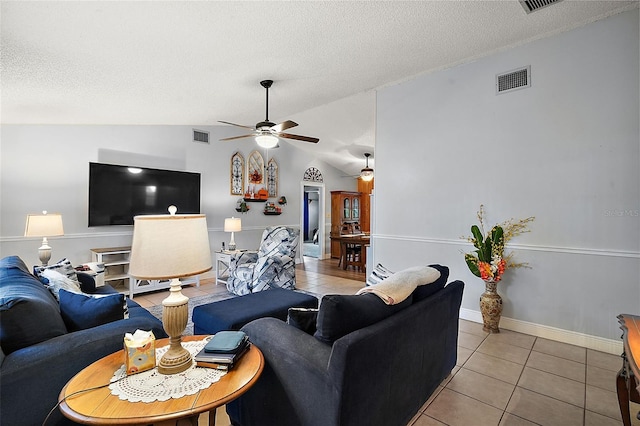 tiled living room with ceiling fan, lofted ceiling, and a textured ceiling