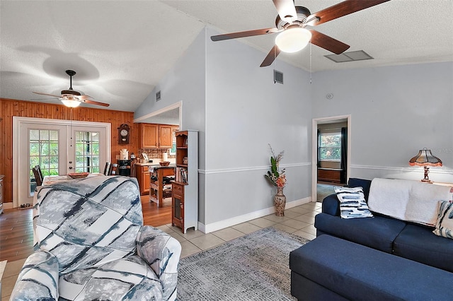 tiled living room with french doors, ceiling fan, lofted ceiling, and wood walls