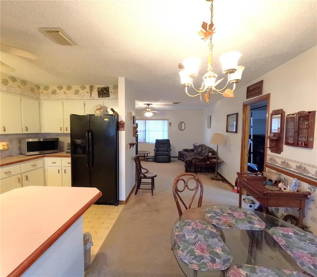 kitchen with white cabinets, ceiling fan with notable chandelier, black fridge, hanging light fixtures, and a textured ceiling