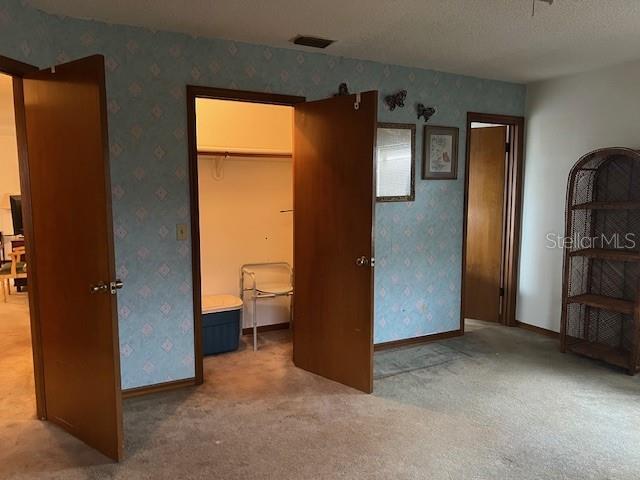 unfurnished bedroom featuring ensuite bathroom, carpet flooring, a spacious closet, a textured ceiling, and a closet