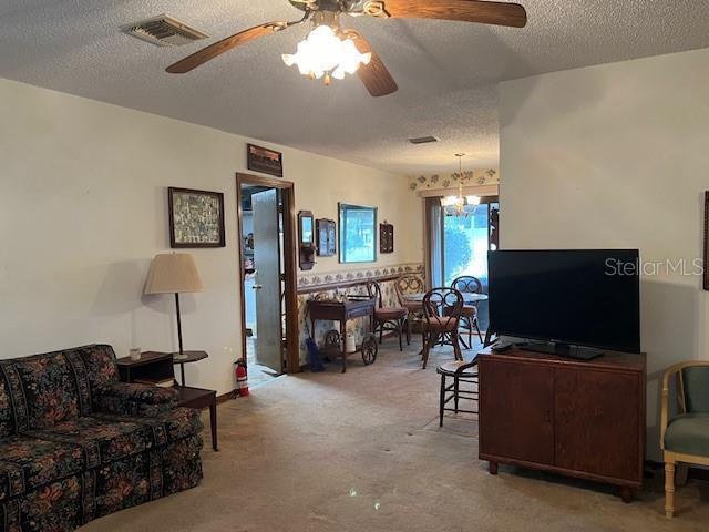 carpeted living room featuring ceiling fan with notable chandelier and a textured ceiling