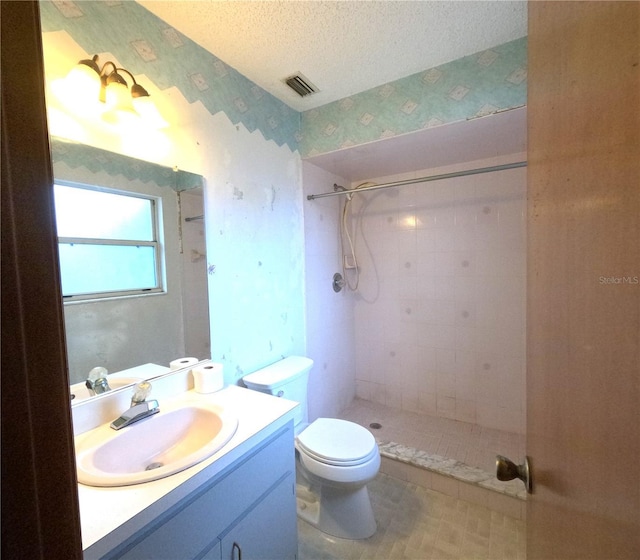 bathroom with toilet, a tile shower, a textured ceiling, and vanity