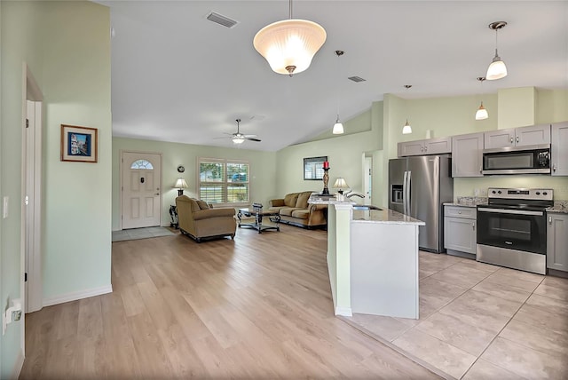 kitchen with gray cabinetry, hanging light fixtures, light hardwood / wood-style flooring, light stone countertops, and stainless steel appliances