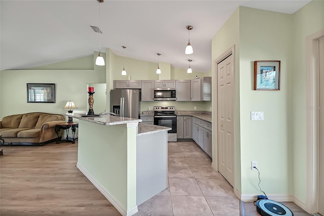 kitchen with hanging light fixtures, vaulted ceiling, light stone countertops, an island with sink, and stainless steel appliances