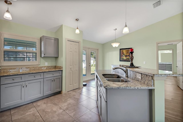 kitchen featuring gray cabinetry, vaulted ceiling, a kitchen island with sink, sink, and decorative light fixtures