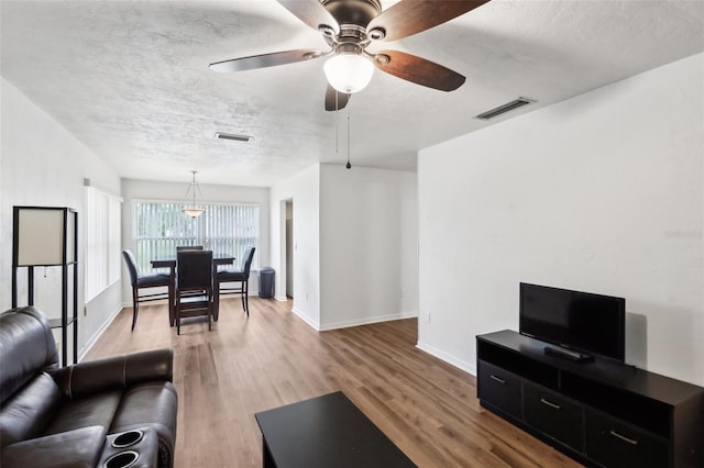 living room featuring hardwood / wood-style flooring, ceiling fan, and a textured ceiling