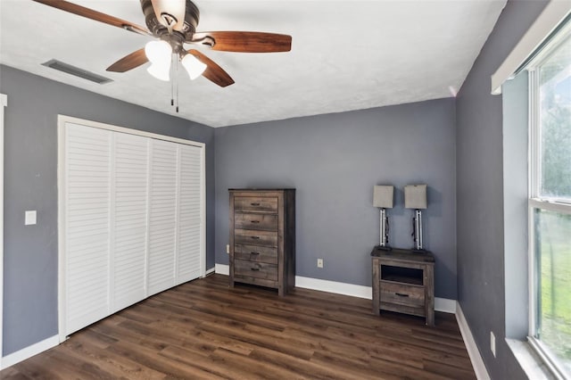 unfurnished bedroom featuring ceiling fan, a closet, dark hardwood / wood-style flooring, and multiple windows