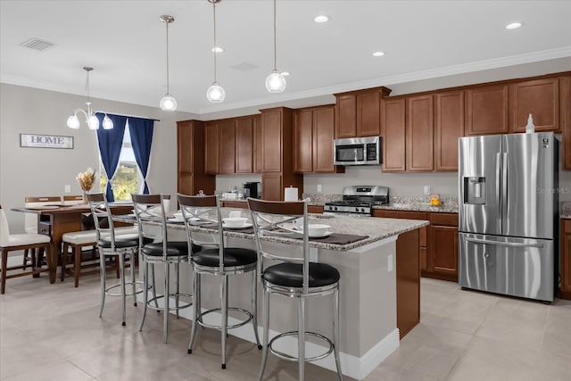 kitchen with ornamental molding, stainless steel appliances, a center island with sink, hanging light fixtures, and a breakfast bar area