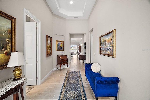 corridor with light tile patterned floors, visible vents, baseboards, a raised ceiling, and a towering ceiling