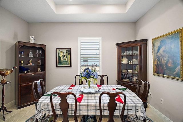 dining room with a raised ceiling, baseboards, and light tile patterned floors