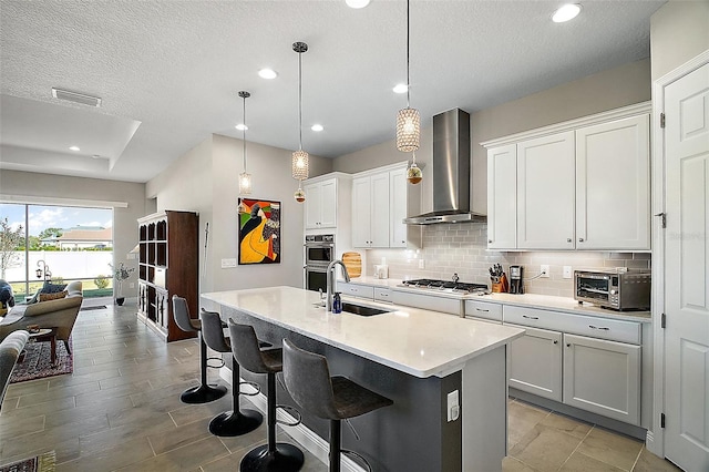 kitchen featuring a toaster, decorative backsplash, wall chimney exhaust hood, light countertops, and a sink