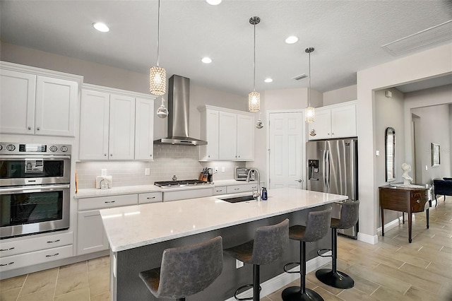 kitchen with tasteful backsplash, wall chimney exhaust hood, appliances with stainless steel finishes, light countertops, and a sink