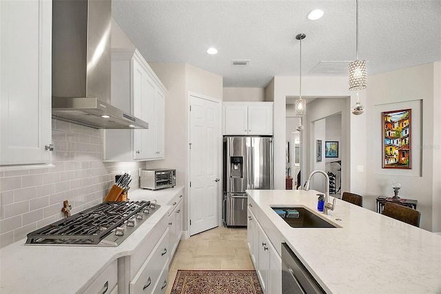 kitchen with decorative backsplash, appliances with stainless steel finishes, wall chimney range hood, white cabinetry, and a sink