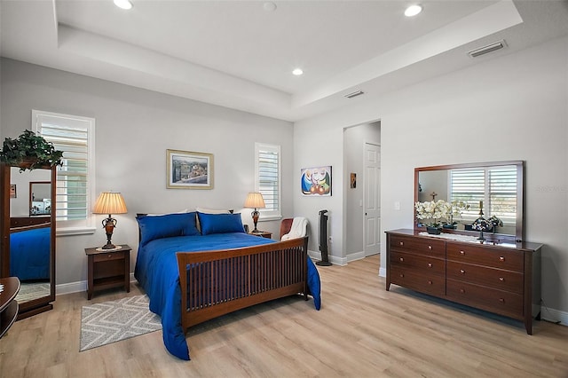 bedroom with baseboards, a raised ceiling, visible vents, and light wood-style floors