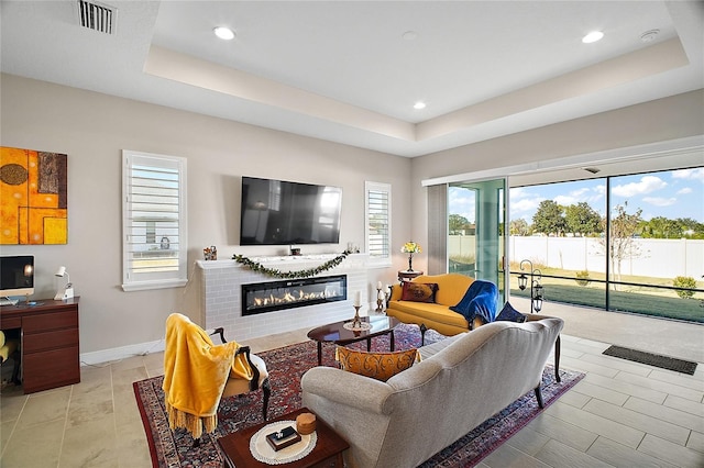 living area with baseboards, visible vents, a tray ceiling, and a glass covered fireplace