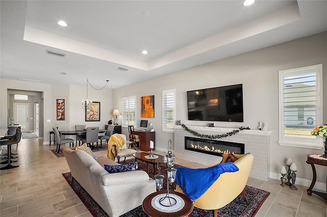 living area featuring recessed lighting, visible vents, baseboards, a tray ceiling, and a glass covered fireplace