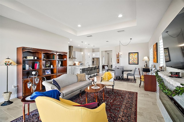 living area with a raised ceiling, visible vents, and recessed lighting