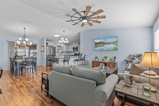 living room with a textured ceiling, light hardwood / wood-style flooring, ceiling fan with notable chandelier, and vaulted ceiling