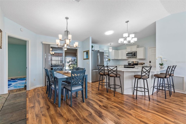 dining space featuring a textured ceiling, dark hardwood / wood-style floors, an inviting chandelier, and vaulted ceiling