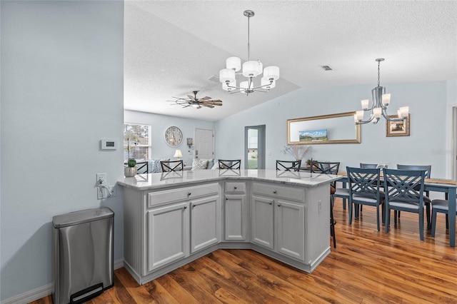 kitchen with dark wood-type flooring, kitchen peninsula, pendant lighting, lofted ceiling, and ceiling fan with notable chandelier