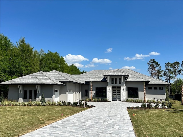 prairie-style home featuring stucco siding, a front lawn, french doors, a garage, and decorative driveway