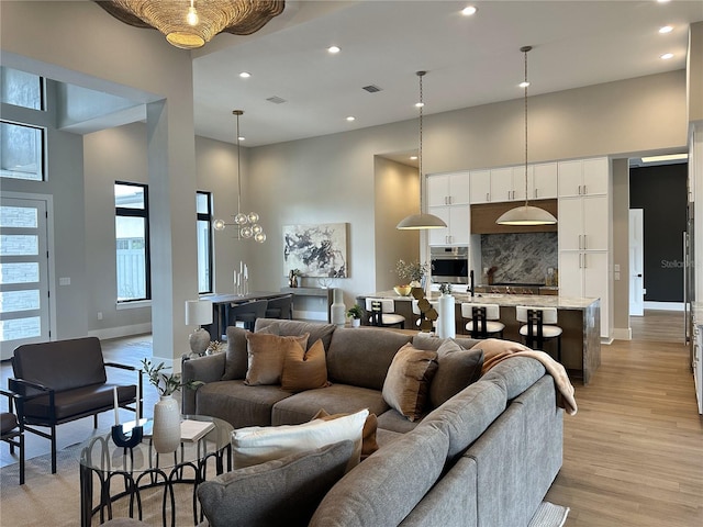 living area with a high ceiling, light wood finished floors, recessed lighting, baseboards, and visible vents