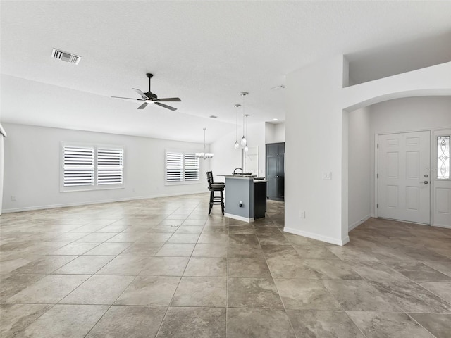 unfurnished living room with a textured ceiling, light tile patterned floors, and ceiling fan with notable chandelier