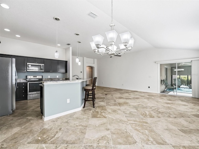 kitchen featuring stainless steel appliances, lofted ceiling, decorative light fixtures, a breakfast bar, and a center island with sink