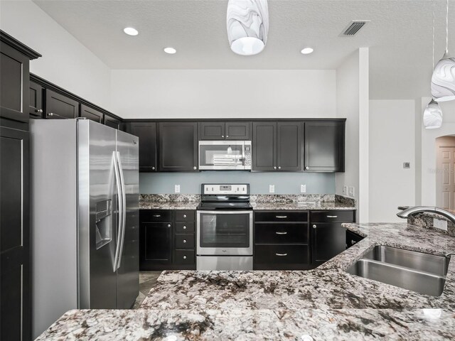 kitchen featuring appliances with stainless steel finishes, light stone counters, pendant lighting, and sink