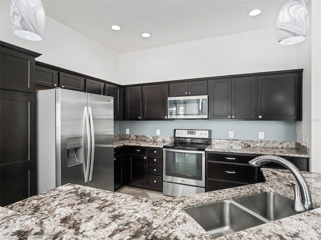 kitchen featuring hanging light fixtures, light stone counters, sink, and stainless steel appliances