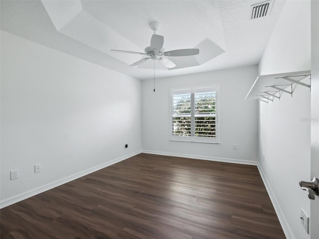 unfurnished room featuring a textured ceiling, dark hardwood / wood-style floors, ceiling fan, and a tray ceiling