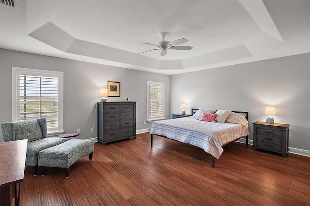 bedroom with ceiling fan, a raised ceiling, and dark wood-type flooring