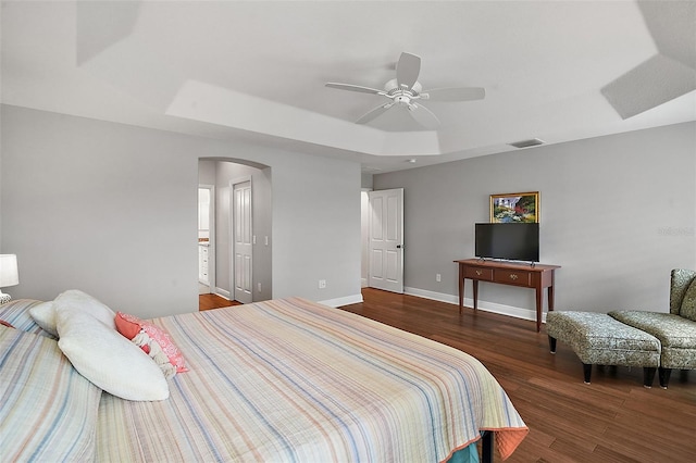 bedroom with ceiling fan, a raised ceiling, and dark wood-type flooring