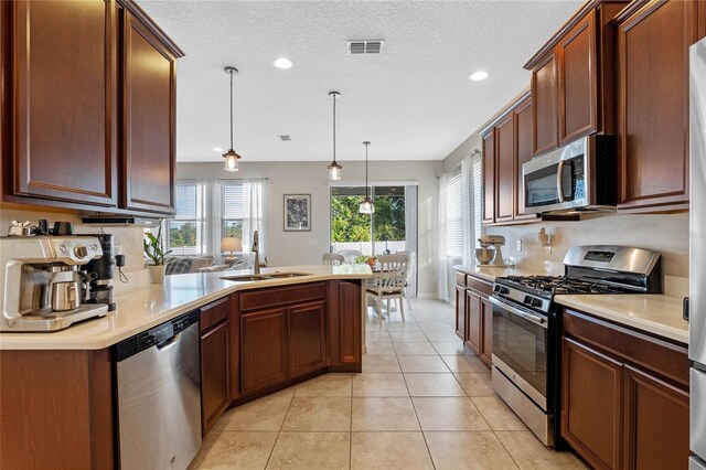 kitchen with a textured ceiling, stainless steel appliances, sink, light tile patterned floors, and hanging light fixtures