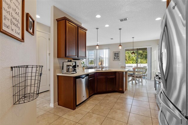 kitchen featuring kitchen peninsula, appliances with stainless steel finishes, a textured ceiling, sink, and decorative light fixtures